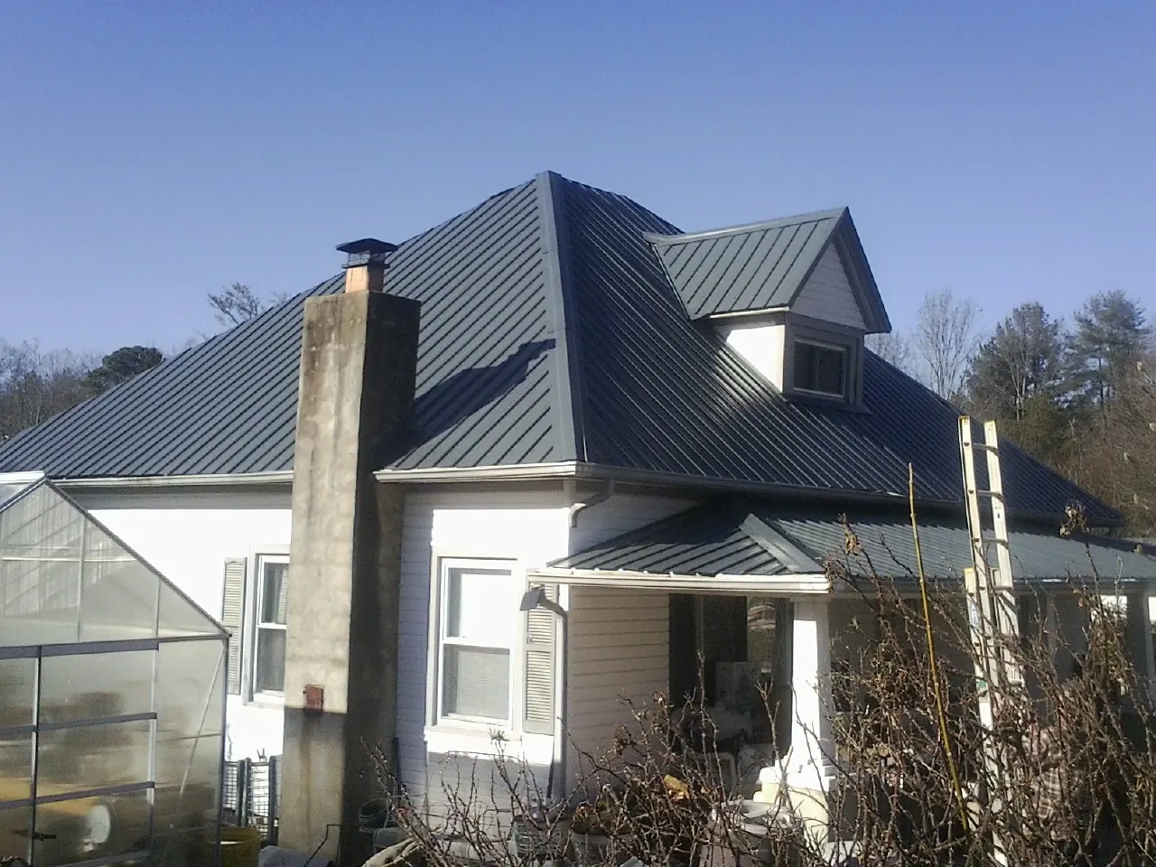 Dark blue standing seam metal roof on a white farmhouse with dormer — Slate & Tile Roof Repair by Roofing Brothers in Colon