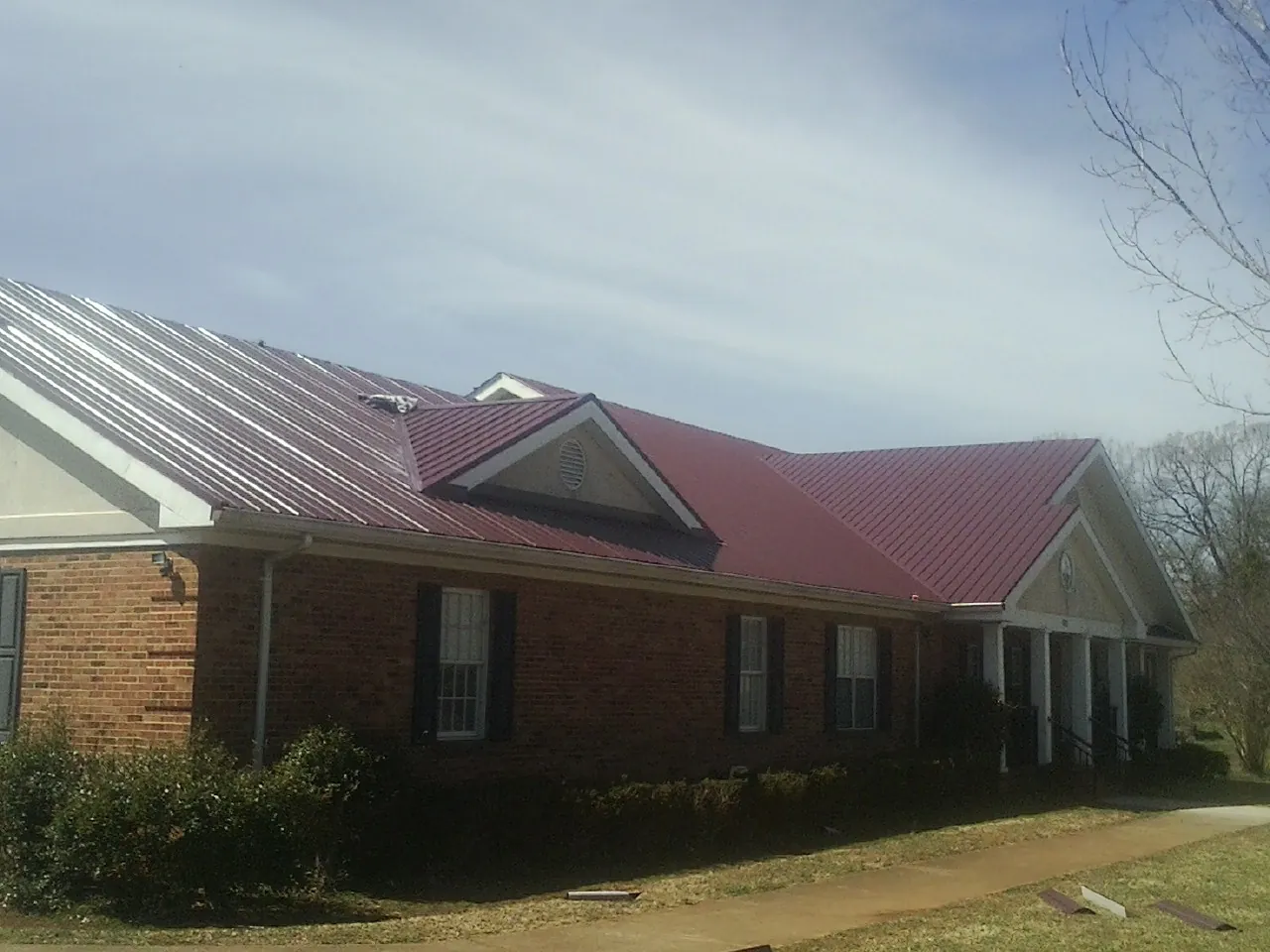 Red metal roof with gabled entries on a long brick building, from a Hail Damage Roof Repair job in Colon