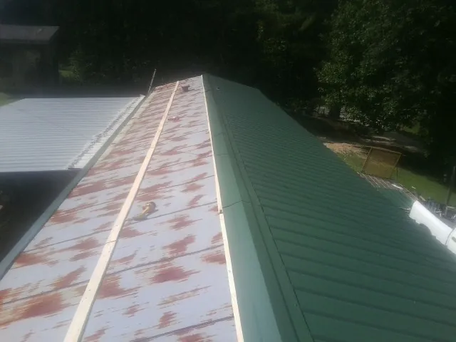 Old rusted panels beside newly installed green metal roofing — Wind Damage Roof Repair by Roofing Brothers in Colon