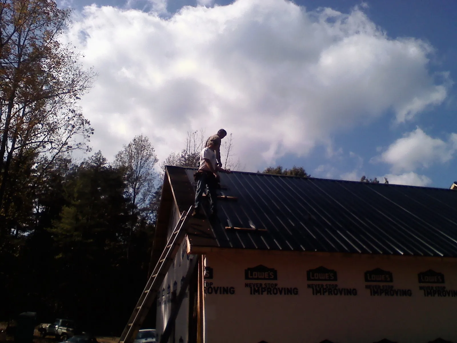 Roofer fastening dark metal panels high against a cloudy sky, from a Roof Inspection job in Colon