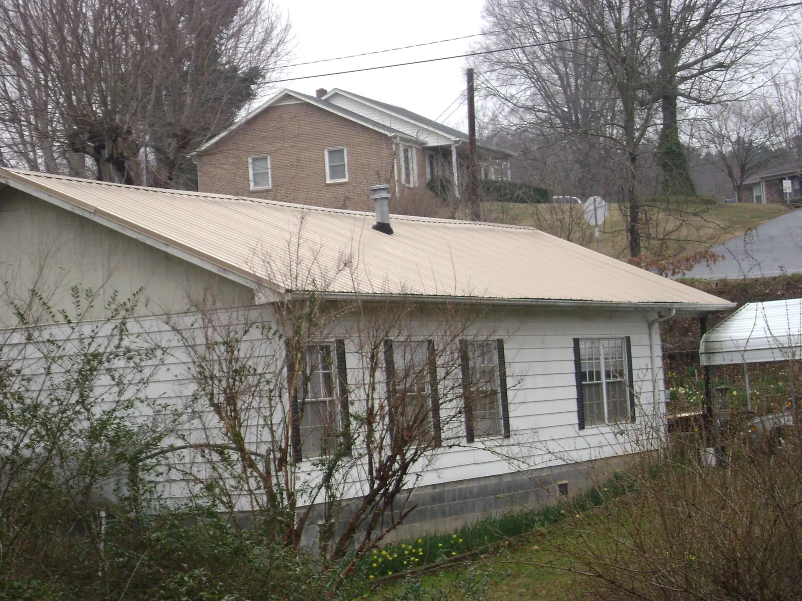 Tan metal roof on a white sided house set into a hillside — Commercial Roofing by Roofing Brothers in Colon