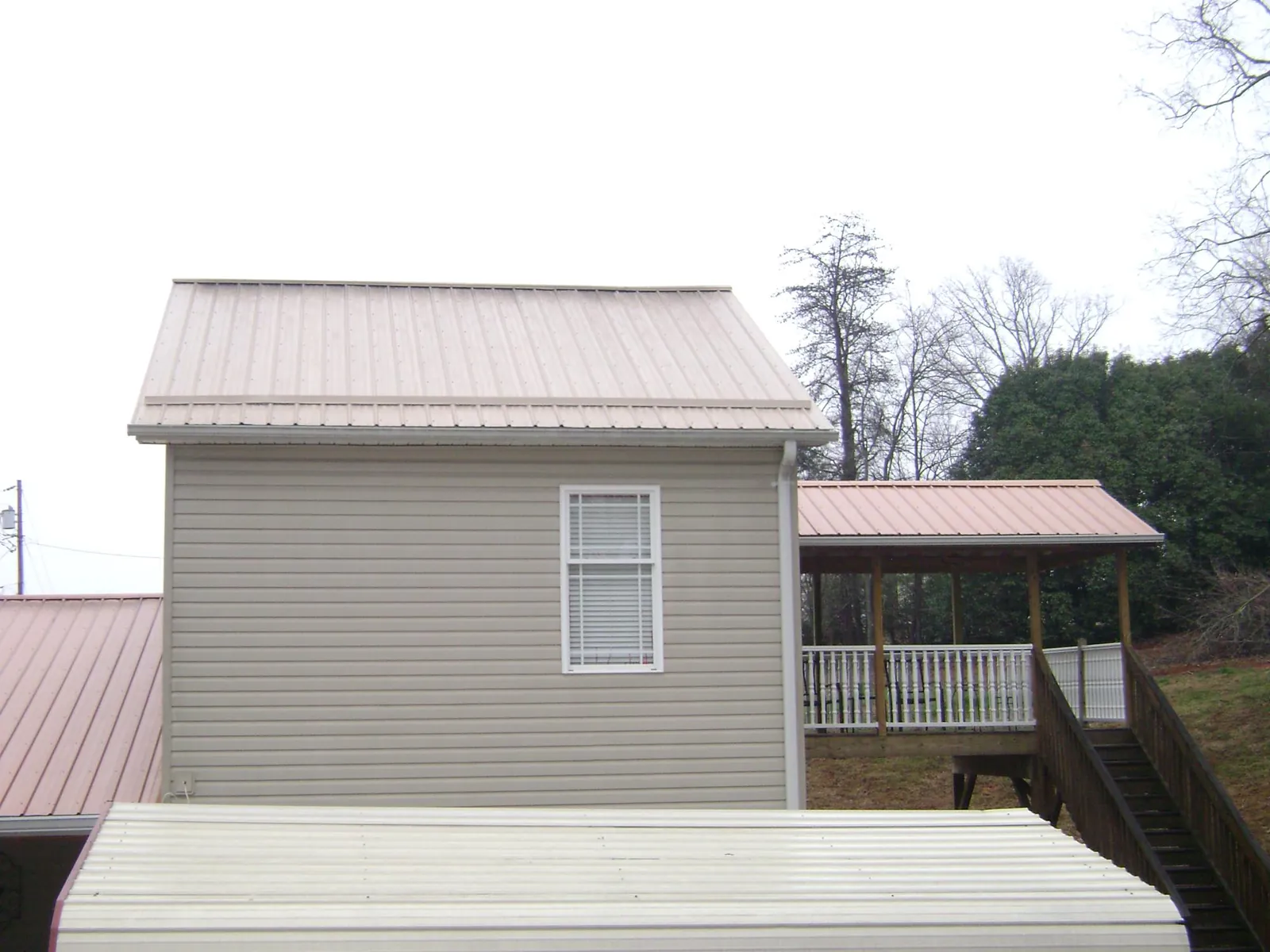 Tan metal roofs on a two story addition and attached porch, from a Roof Replacement job in Colon